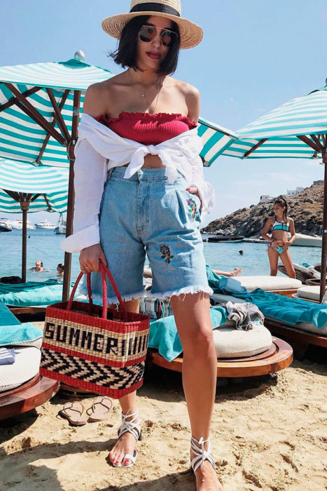 Chica con bermudas de mezclilla, top rojo y camisa blanca atada a la cintura