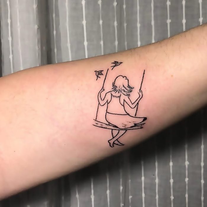 Tatuaje al estilo hand poke de una niña columpiándose en un columpio con un par de aves alrededor
