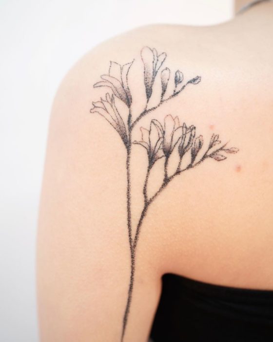 Tatuaje al estilo hand poke de flores y botones de flores en el área del omóplato