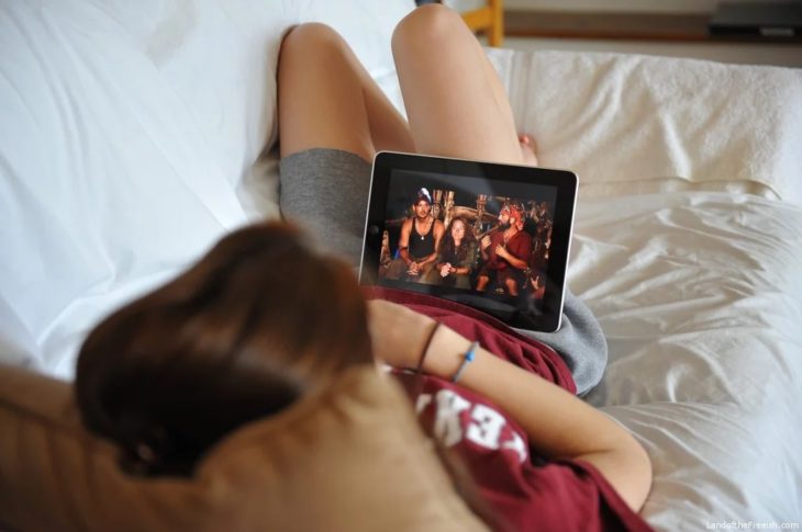 Chica recostada en una cama viendo series