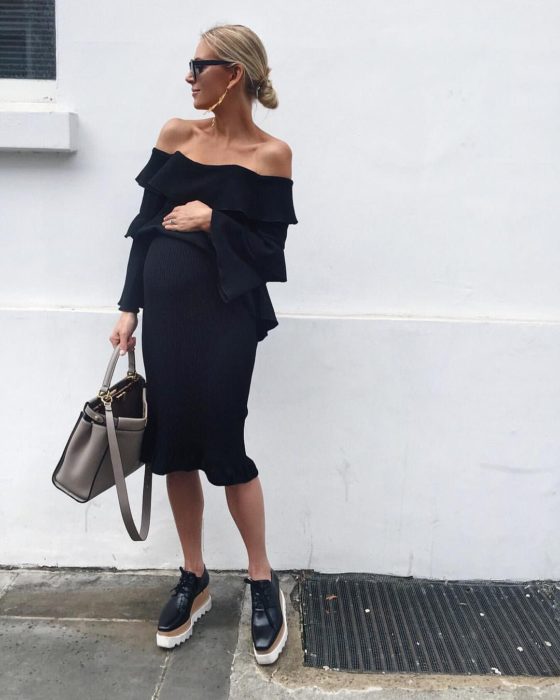 Chica embarazada usando un vestido negro con zapatos de plataforma