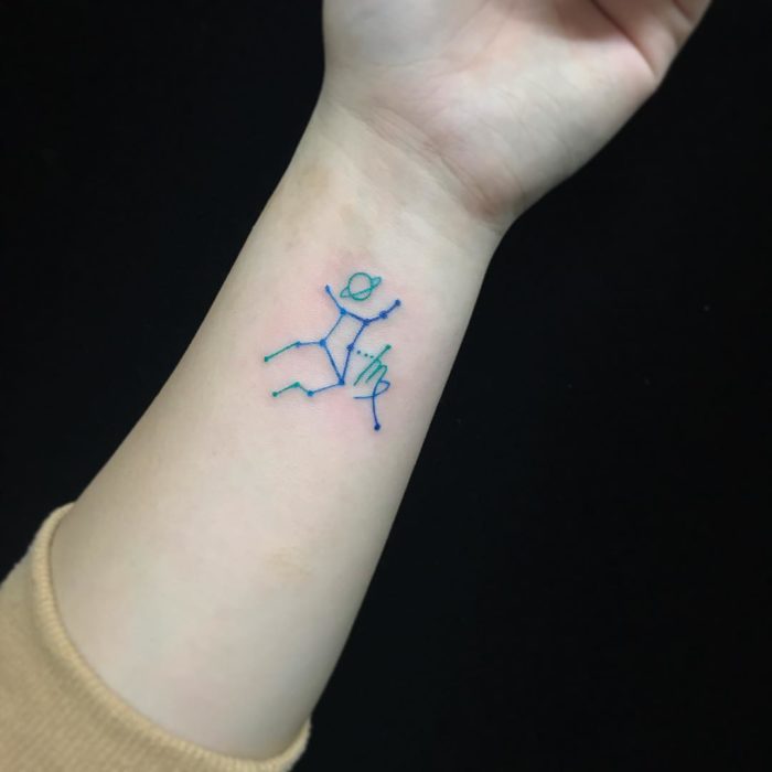 Tatuaje de la constelación de Virgo en tinta azul en la muñeca