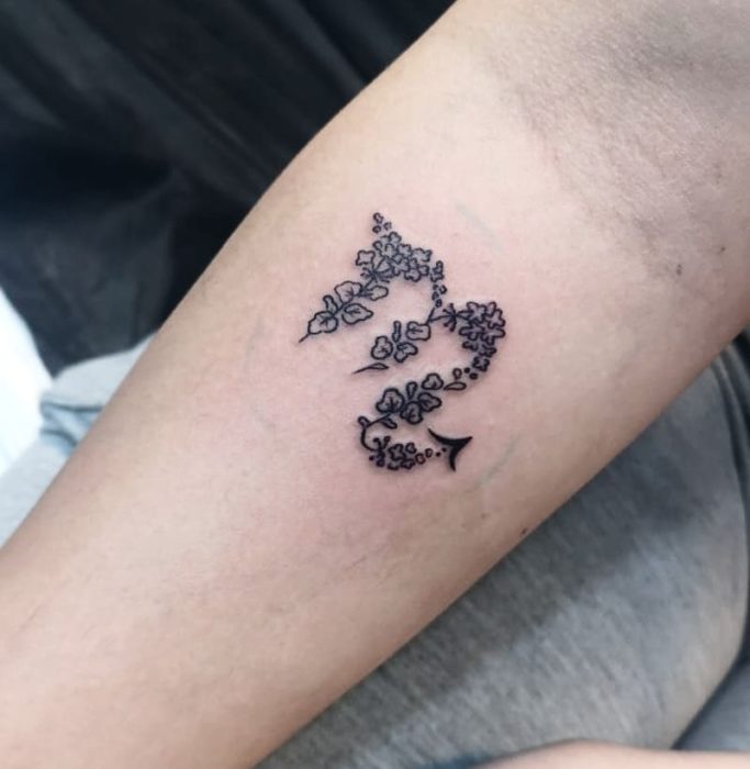 Tatuaje del símbolo de Escorpio a tinta negra con flores en el antebrazo