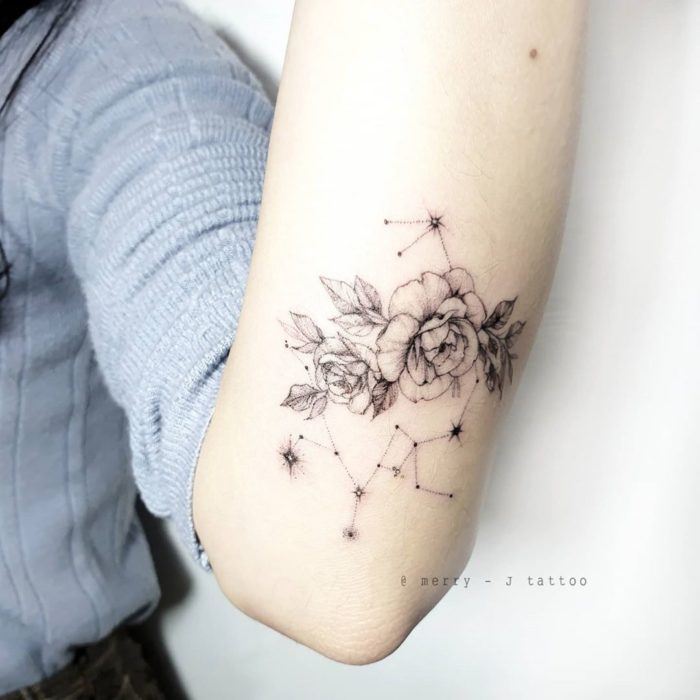 Tatuaje de la constelación de Sagitario adornada con flores en el antebrazo en tinta negra