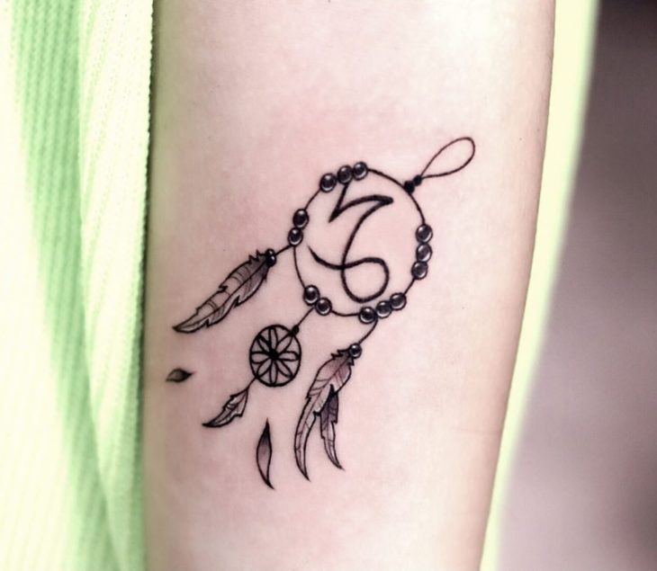Tatuaje del símbolo de Capricornio y un atrapasueños en el antebrazo