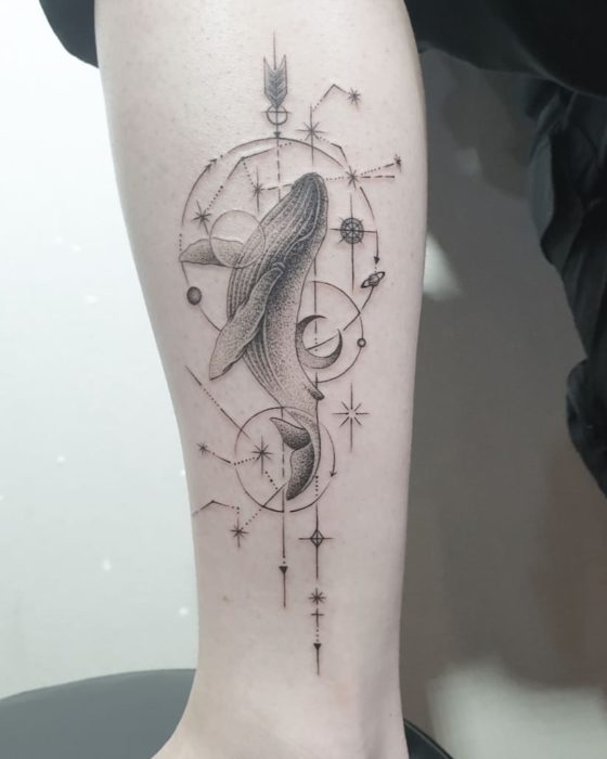 Tatuaje de la constelación de Acuario con una ballena sobre ella y otros detalles en tinta negra en el antebrazo
