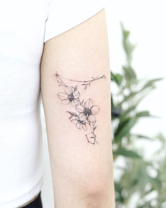 Tatuaje de la constelación de Piscis en la parte trasera del brazo decorada con flores en tinta negra