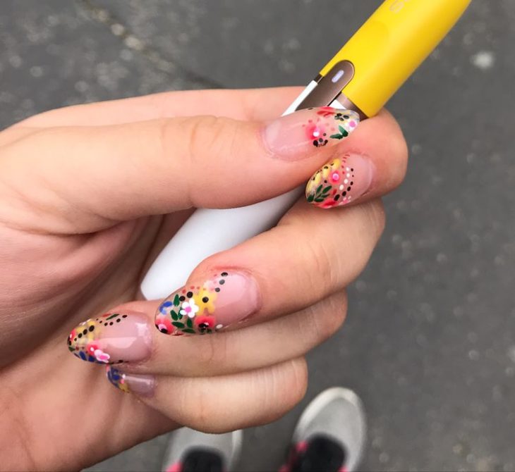 Manicura estilo francés con flores de colores amarillos, naranjas y rojas