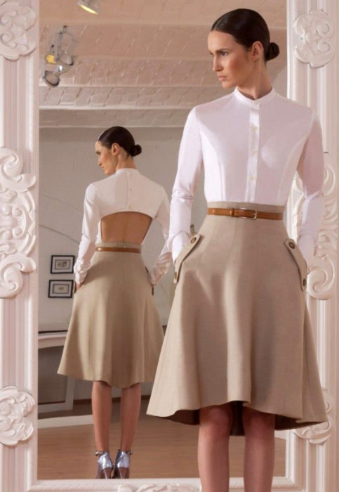Outfit con blusa blanca; mujer mirándose al espejo, con peinado de chongo elegante, camisa blanca sin espalda y falda beige