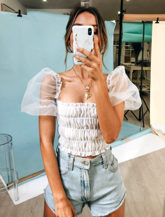 Mujer tomándose un selfie frente al espejo con top blanco de mangas gigot y short