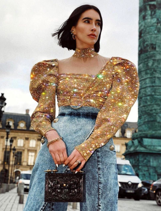 Mujer de cabello corto con blusa dorada brillante y mangas gigot, con mom jean a la cintura