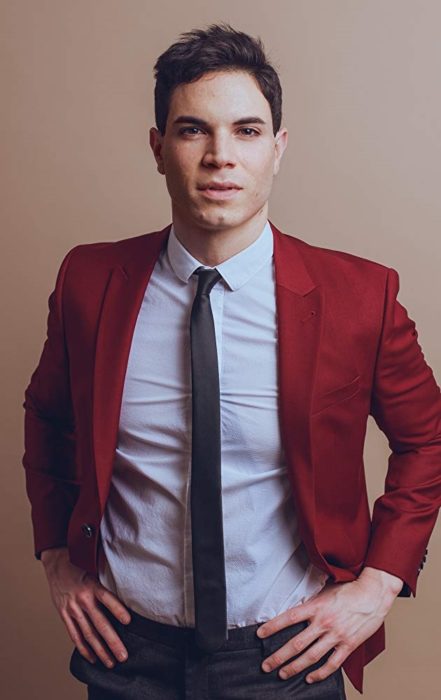 Jason Gotay modelando un saco en tono rojo con jeans azules