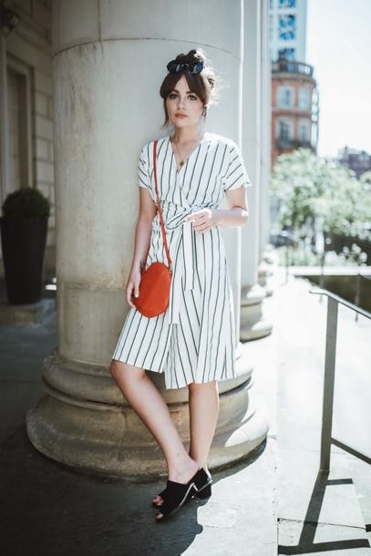 Chica recargada en un pilar con vestido blanco a rayas negras estilo wrap