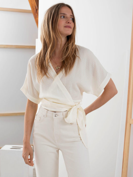 Wrap tops o blusas cache coeur blanca con pantalón blanco a la cintura; mujer con cabello rubio ombré despeinado