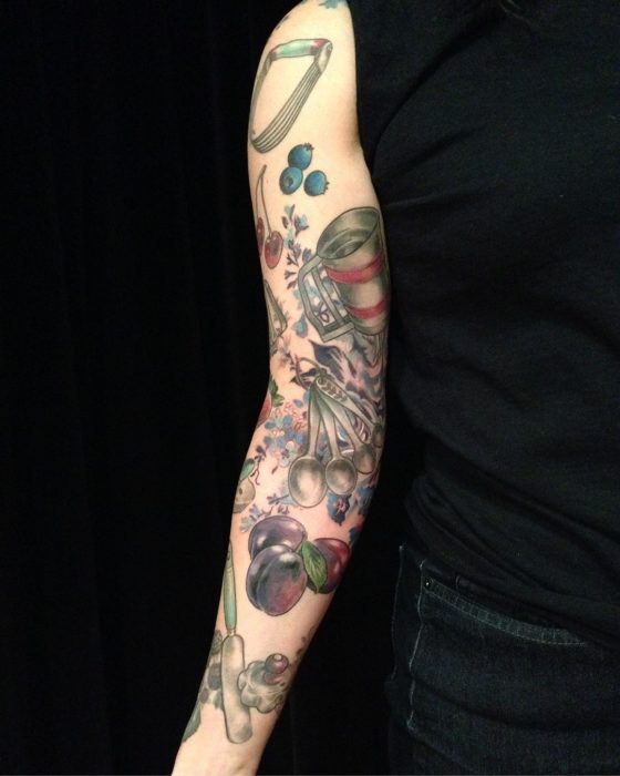 Tatuaje a lo largo del brazo con frutillas y utensilios de cocina