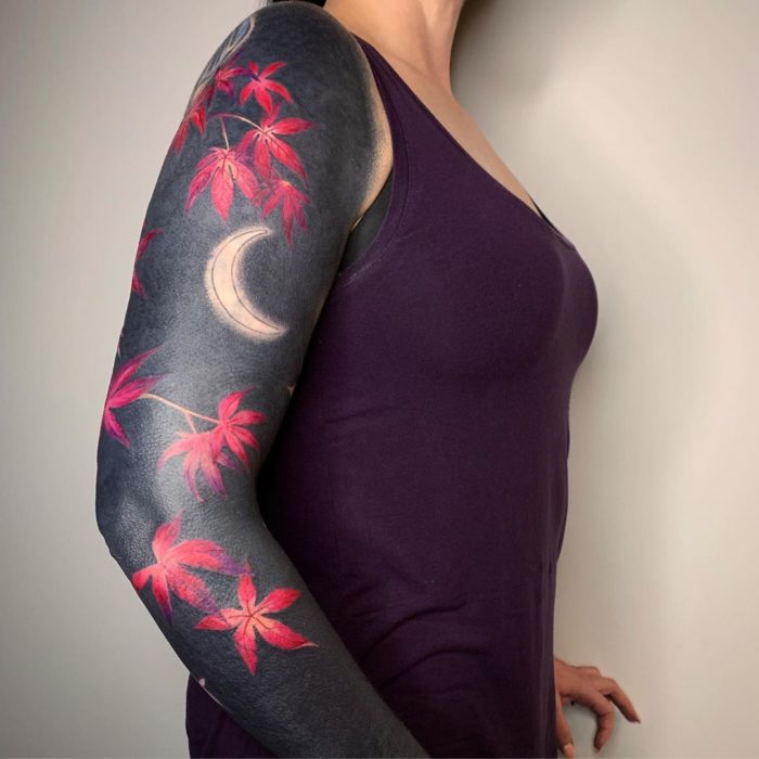 Tatuaje tipo manga en fondo negro y hojas de árbol de color rojo