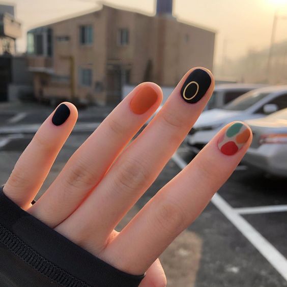 Manicura en uñas cortas con tonos negro, naranja y colores neutros
