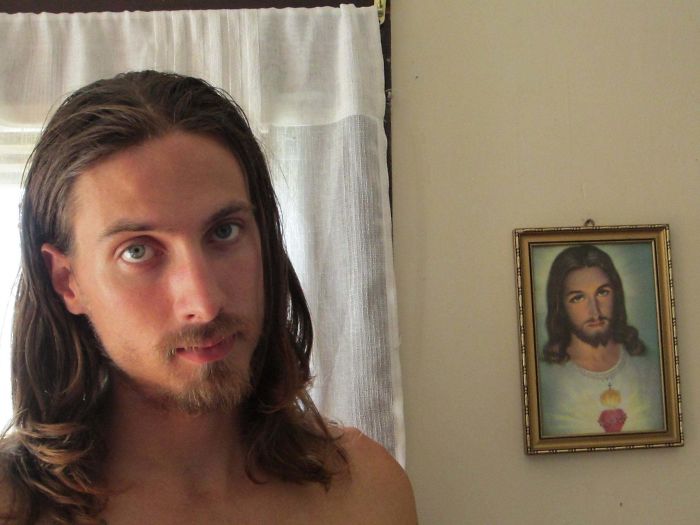 Chico con cabello largo posando junto a la imagen de Cristo
