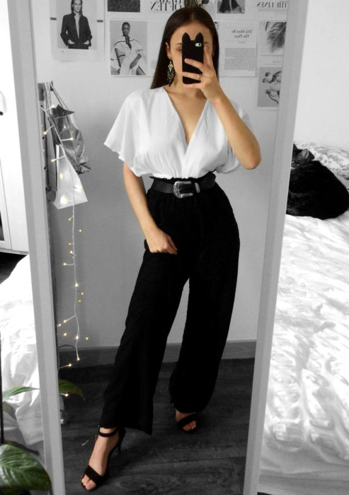 Atuendos formales y juveniles para oficina; mujer tomando una selfie frente al espejo, blusa blanca holgada, pantalón de vestir negro y cinto estilo vaquero