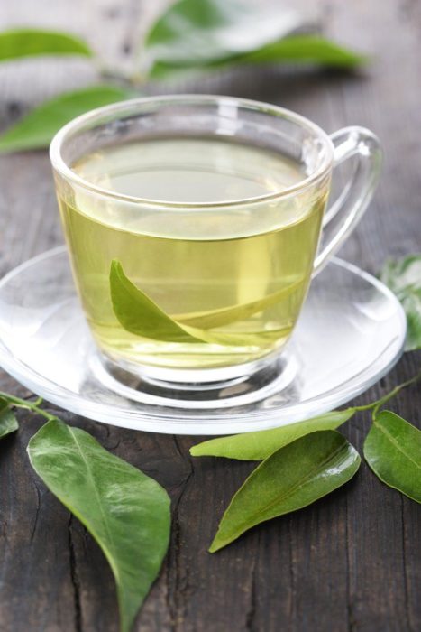 Té verde en taza de cristal sobre mesa de madera oscura con hojas de té adornando