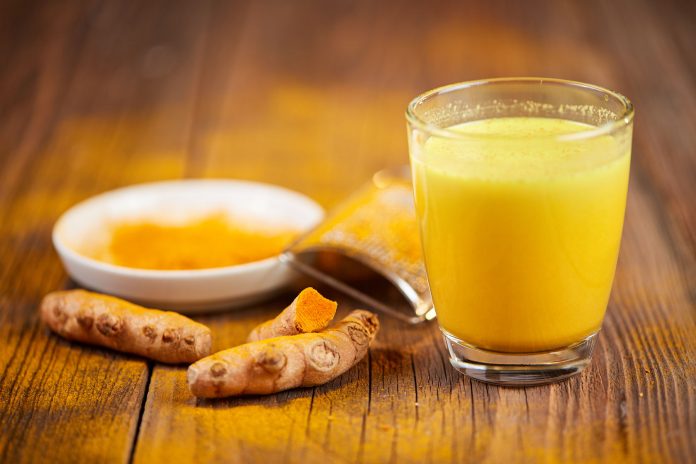Infusión de cúrcuma en vaso de cristal con cúrcuma fresca y en polvo adornando sobre mesa de madera