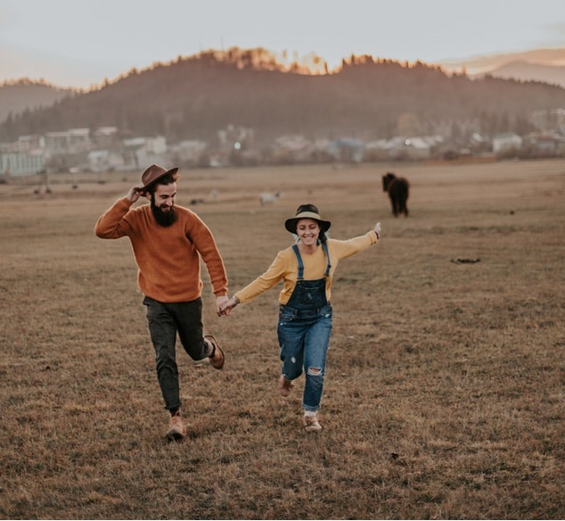 Pareja de novios corriendo por el campo tomados de la mano