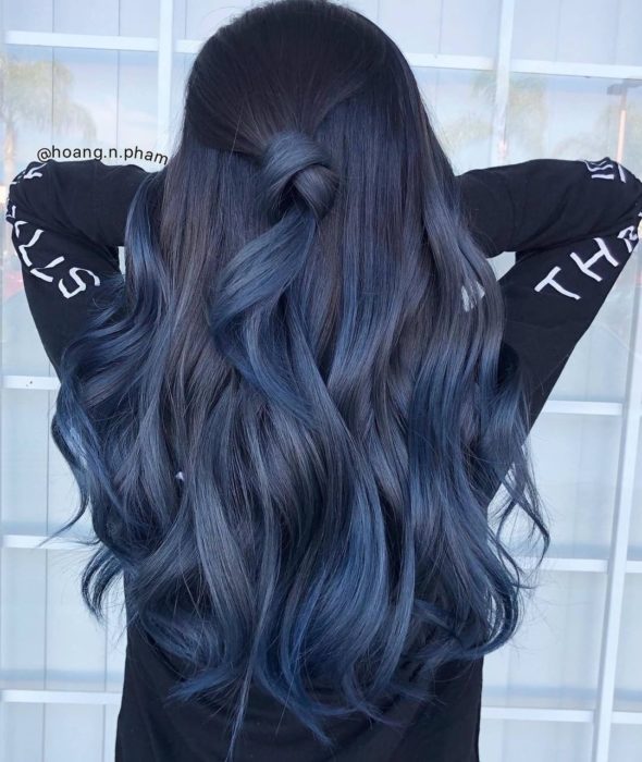 Chica con el cabello teñido de azul mezclilla sujetado en una coleta media y rizos
