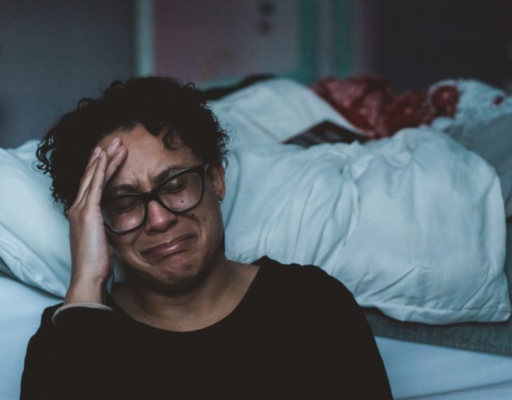 Mujer de lentes y cabello desordenado llorando en su habitación