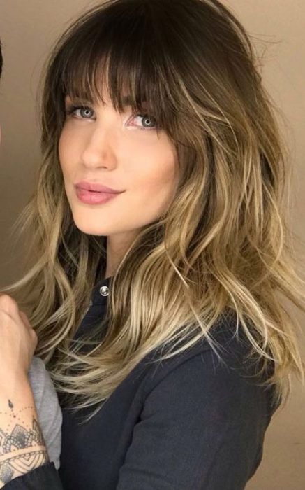 Chica con cabello rubio, sonriendo, posando de perfil, con corte estilo shag