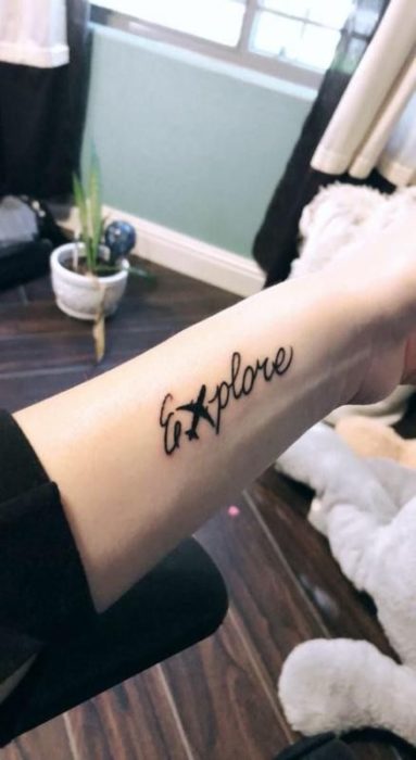 Tatuaje en el antebrazo con la palabra explore y un avión al centro