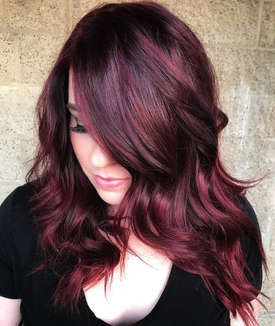 Chica con peinado en ondas ligeras teñido en cherry wine y mirando hacia abajo