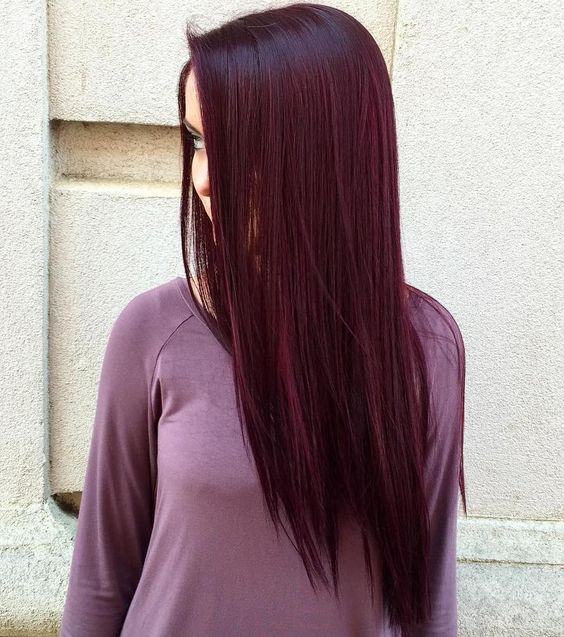 Chica de cabello extralargo volteada de perfil modelando su teñido en cherry wine