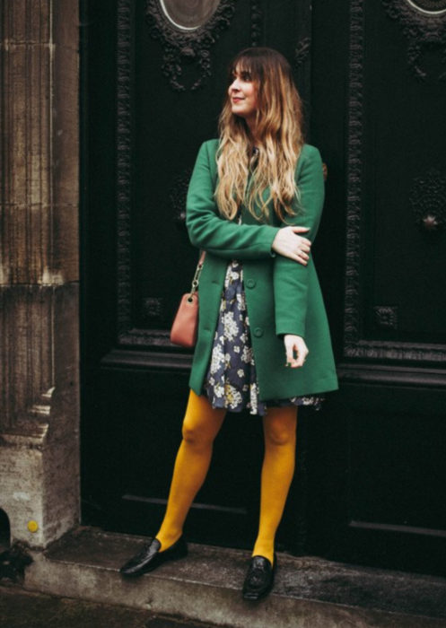 Outfits con medias de colores; chica posando frente a puerta, con medias amarillas, vestido de flores y saco verde