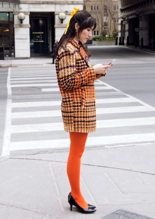 Outfits con medias de colores; chica con medias naranjas y saco de cuadros, mirando su celular en la calle