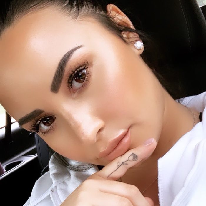 Demi Lovato mostrando su tatuaje de rosa en el dedo meñique