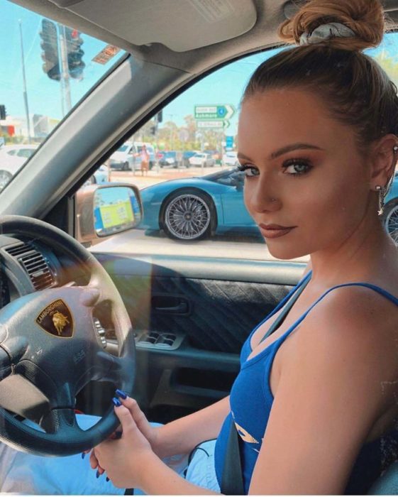 Chica sentada en su auto afirmando que se trata de un Ferrari