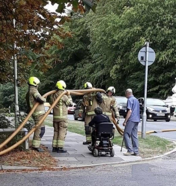 Bomberos ayudando a un hombre en silla de ruedas a cruzar la calle
