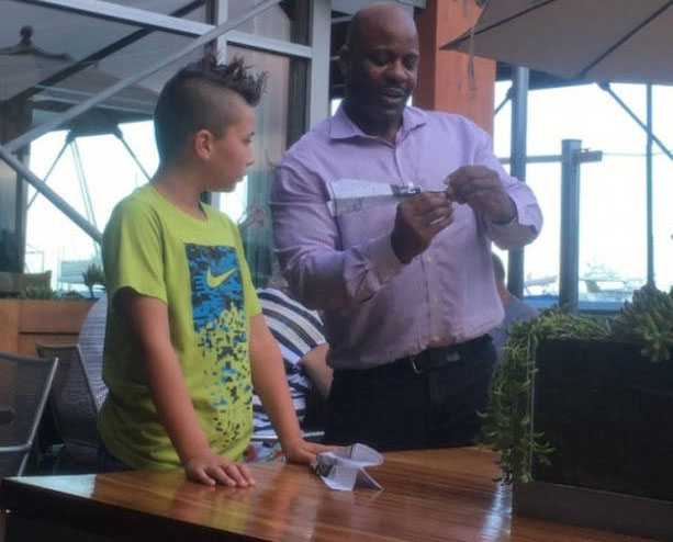 Empleado de restaurante ayuda a un chico a hacer un avión de papel