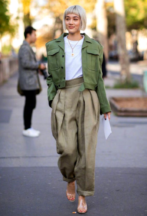 Mujer con cabello rubio y flequillo, usando pantalones y saco oversized