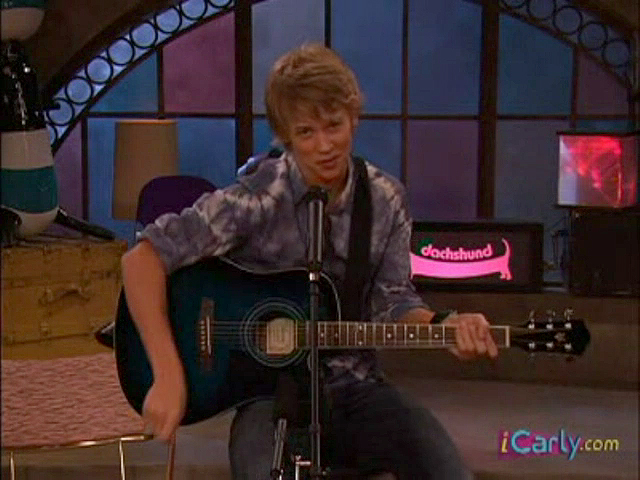 Austin Butler sentado en un banquito tocando guitarra en iCarly