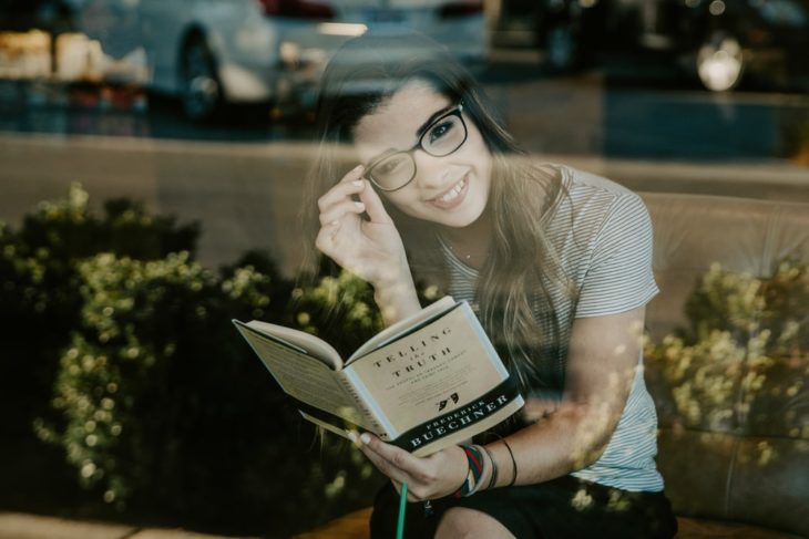 Chica leyendo un libro en una cafetería y sonriendo