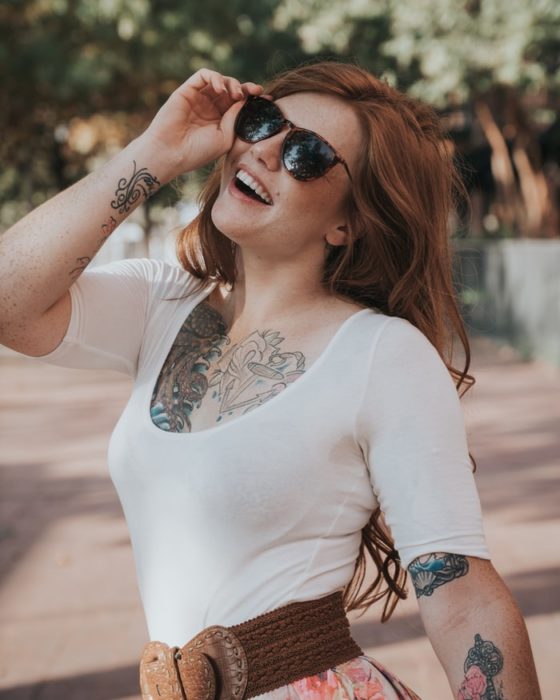 Chica con tatuajes sonriendo y usando gafas oscuras