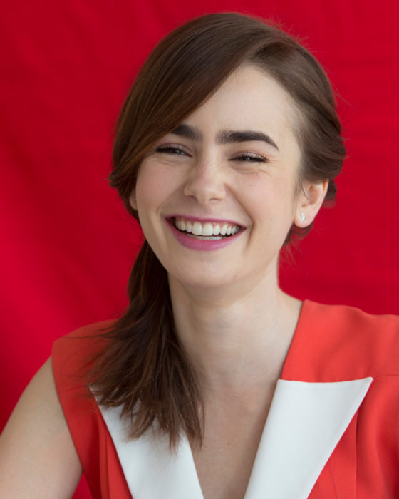 Peinados de Lily Collins para Año Nuevo; mujer de cabello lacio, mediano, castaño recogido en una coleta de lado, chica riendo