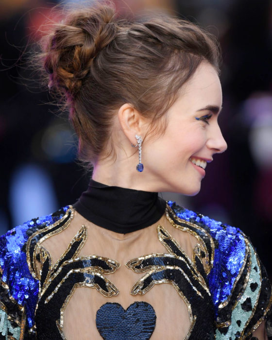 Peinados de Lily Collins para Año Nuevo; mujer de cabello largo y castaño, con peinado de chongo y trenzas románticas, vestido de lentejuelas azul con corazón negro