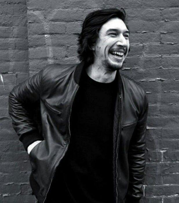 Actor Adam Driver; fotografía en blanco y negro de un hombre sonriendo, con chamarra de cuero, cabello largo y oscuro, barba y bigote