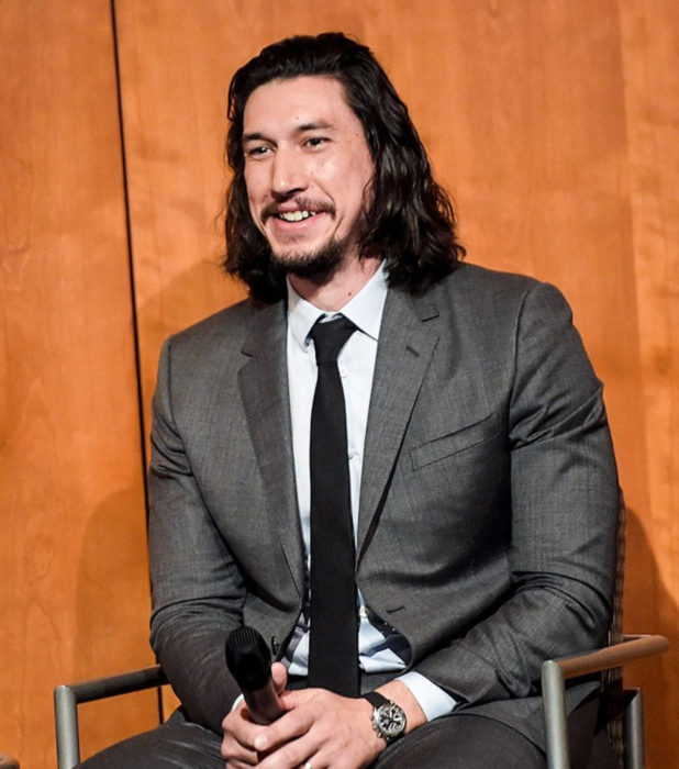 Actor Adam Driver; hombre sentado con un micrófono en mano, cabello largo y negro, barba y bigote