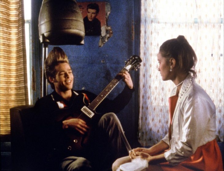 Brad Pitt con un peinado alto y sentado mientras toca la guitarra