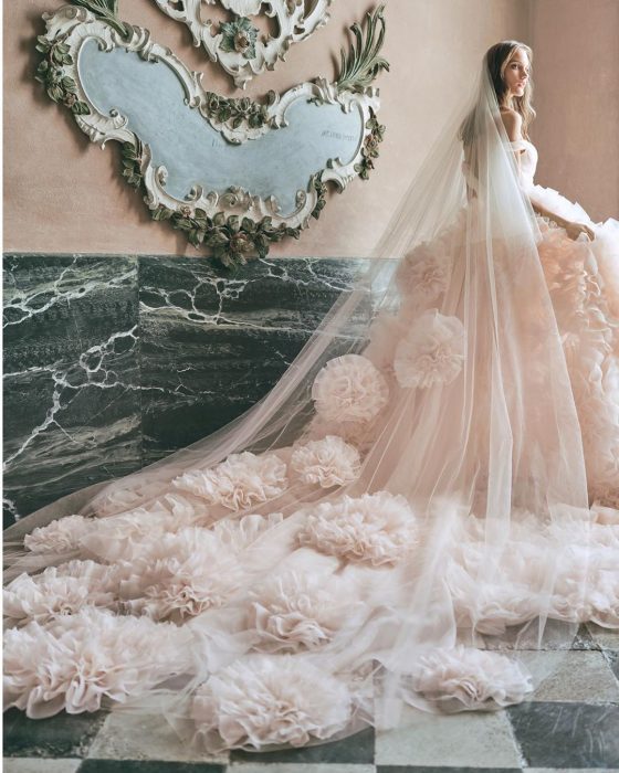 Chica con un vestido de novia blanco con estampado floral y un velo largo con pompones