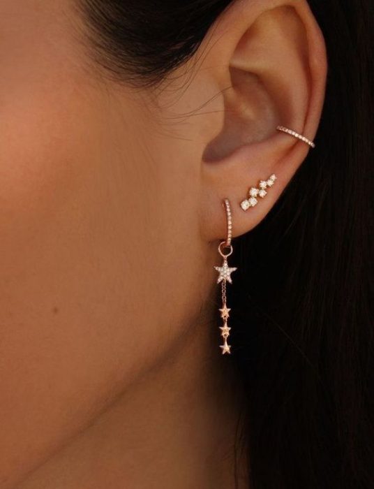 Chica mostrando sus pendientes largos con estrellas doradas y serpientes