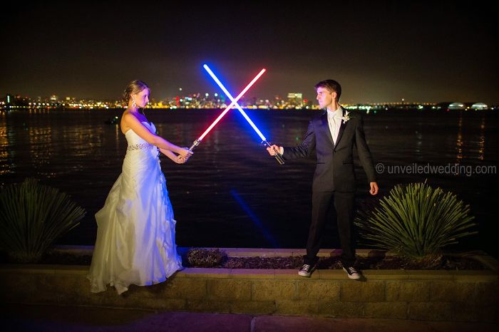 Novios sosteniendo sables de luz mientras posan para la sesión de fotos de su boda